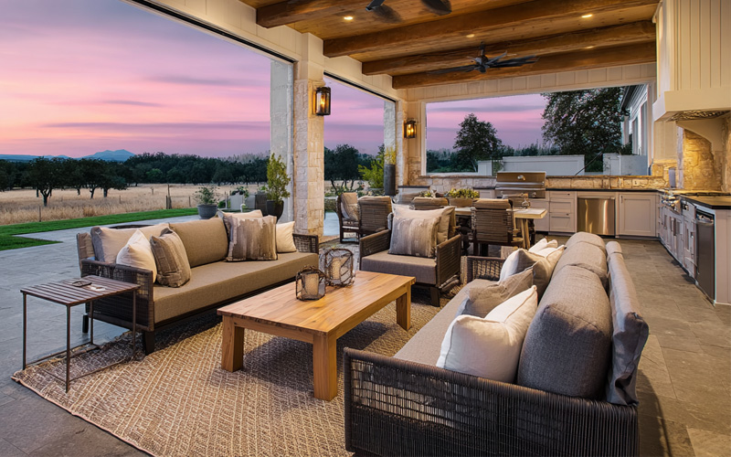 services_0000_Layer 8 Covered outdoor living area with lounges, a timber coffee table and an outdoor kitchen at sunset