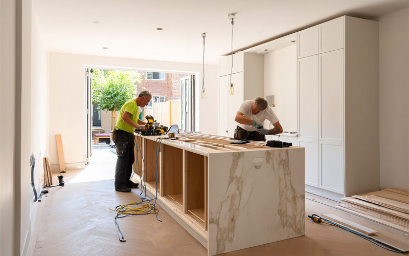 services_0005_Layer 3 Two tradesmen working on a kitchen renovation with a marble-look island bench